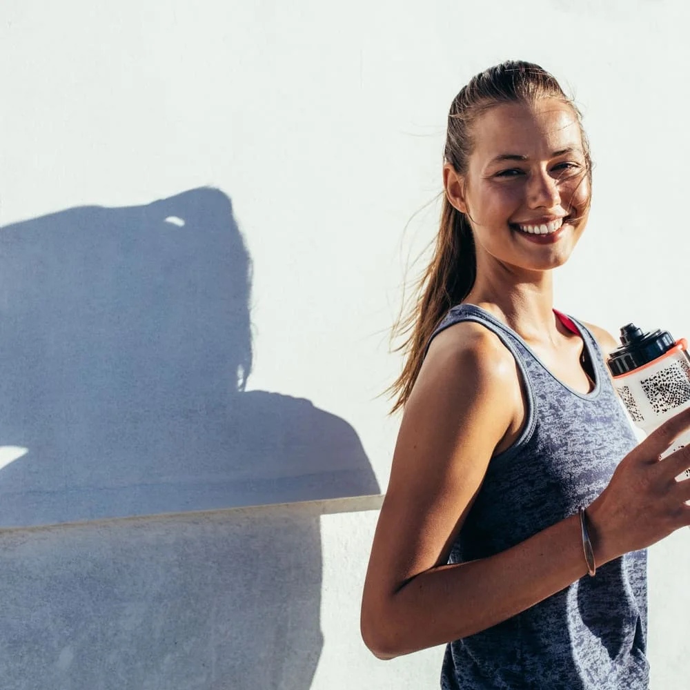 Woman smiling with a water bottle after an active workout